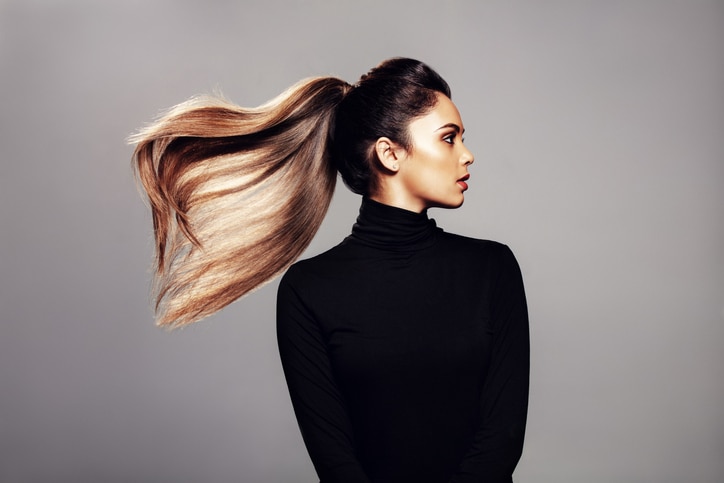 Studio shot of stylish young woman with flying hair against grey background. Female fashion model with long hair.