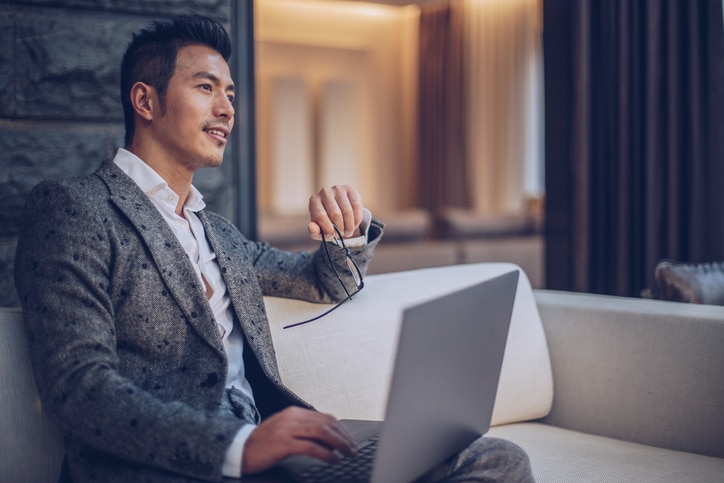 One man, sitting on sofa outdoors, using laptop.