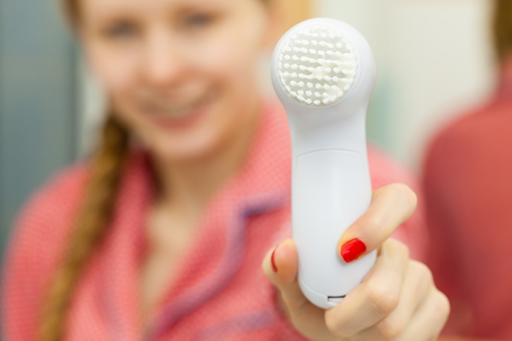 Deep cleaning face tools concept. Woman holding and presenting facial cleansing brush machine.