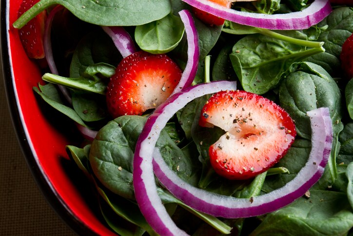 Delicious fresh spinach salad with red onion, ripe strawberries and cracked black pepper.