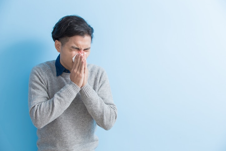 man is sick and sneezing with blue background, asian