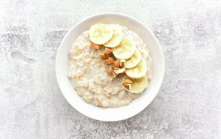 Oats porridge with banana slices and nuts in bowl over stone background. Diet healthy nutrition food concept. Top view, flat lay