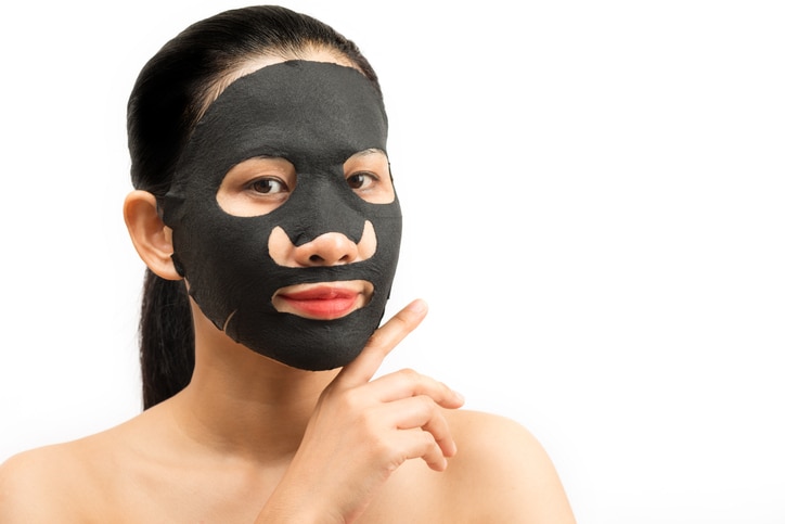 Young woman doing facial black mask sheet with purifying mask on her face