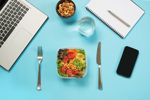 Healthy business lunch in office, salad for snack, almonds, water on blue table. Top view with copy space. Concept healthy nutrition. Lunchbox. To do list.