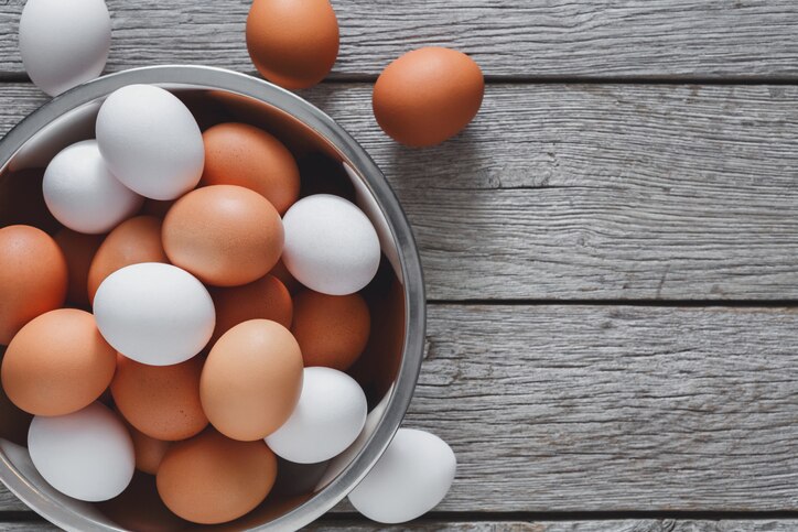 Fresh brown and white eggs in steel bowl on rustic wood background with copy space. Top view. Natural healthy organic food, cooking concept