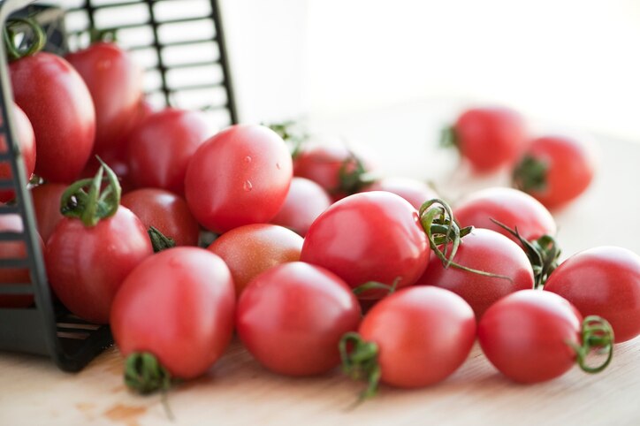 wet red cherry tomatoes in plastic basket on wooden background