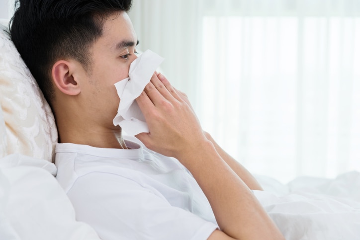 Sick man blowing his nose in bed.