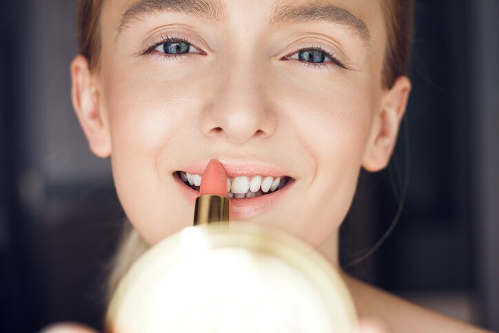 Close up detail of young woman with nice clean and soft skin applying red lipstick on her perfect sexy plump lips.