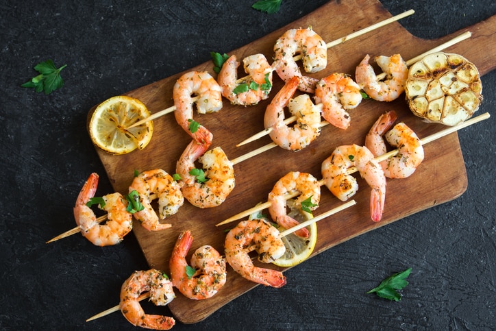 Grilled shrimp skewers. Seafood, shelfish. Shrimps Prawns skewers with herbs, garlic and lemon on black stone background, copy space. Shrimps prawns brochette kebab. Barbecue srimps prawns.