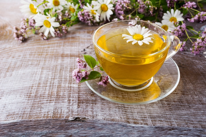 Glass cup of green camomile tea and wild herbs on the rustic wooden background. Herbal organic tea as wellness and relax concept