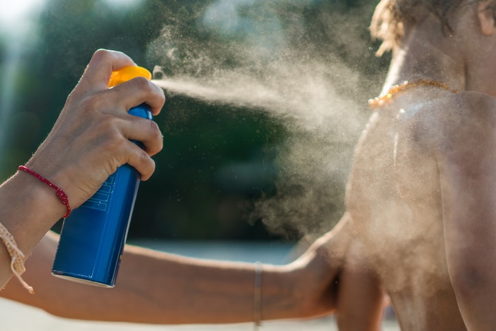 Unrecognizable mother spraying suntan lotion on her son's body at the beach.