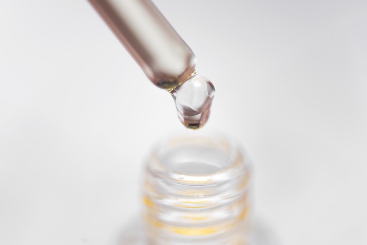 Cuticle oil bottle and a pipette with oil drop close up on a white background. Fingernail care concept.