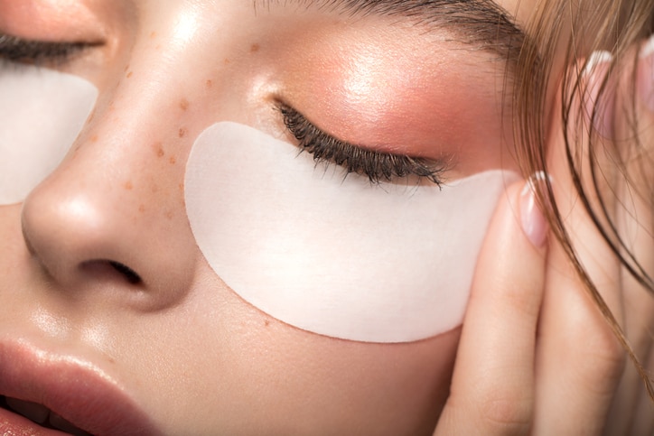 Closeup studio shot of a beautiful young woman with freckles skin and under eye mask posing against a grey background