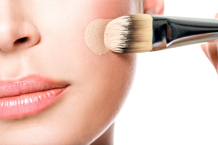 Makeup artist applying liquid tonal foundation  on the face of the woman. Closeup photo of cheek