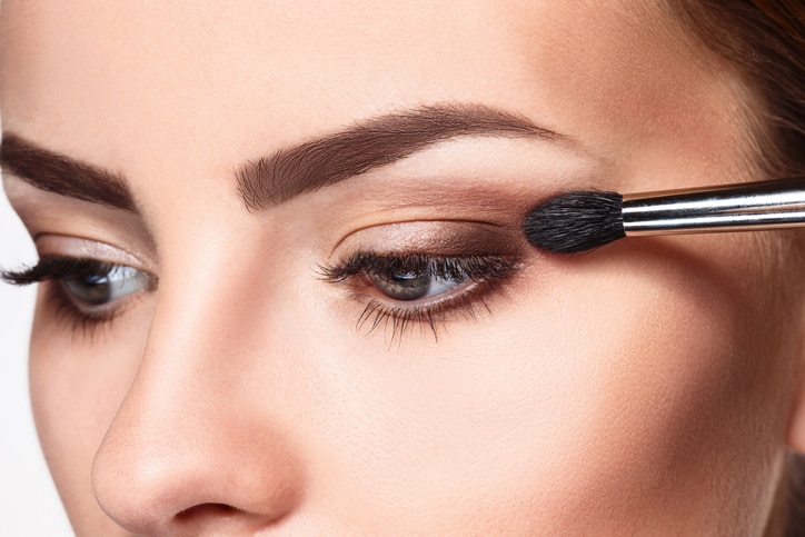 Beautiful female eyes with make-up and brush on white