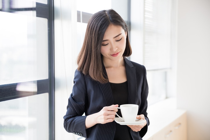 pretty chinese woman wearing a black suit, she is drinking coffee