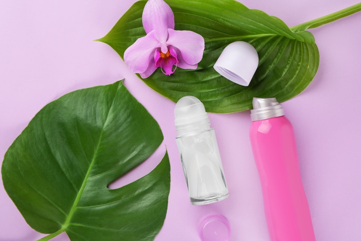 Different deodorants with orchid flower and leaves on color background