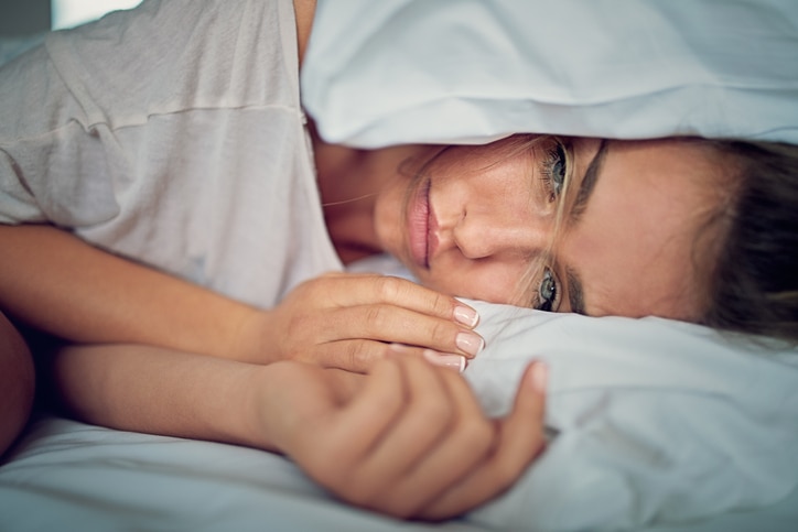 Young girl with relationship difficulties is crying and holding her head under the pillow