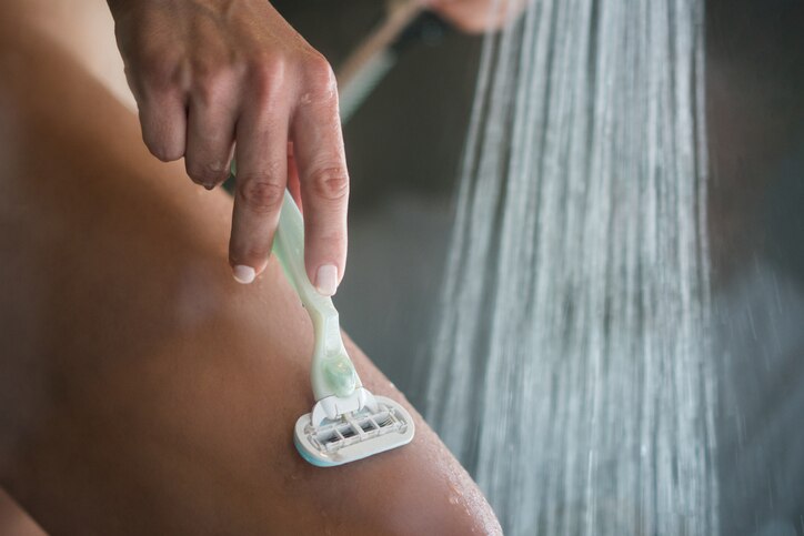 Close up of unrecognizable woman shaving leg with razor during morning shower in the bathroom.