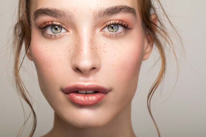 Closeup studio shot of a beautiful young woman with freckles skin posing against a grey background