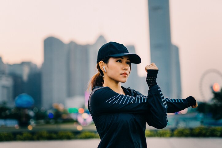 Confidence and determined Asian sports woman stretching arms outdoors against urban city skyline