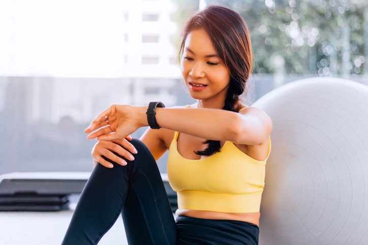 Close up of young Asian active fit woman in sports bra checking smartwatch inside gym - modern technology fitness lifestyle concept