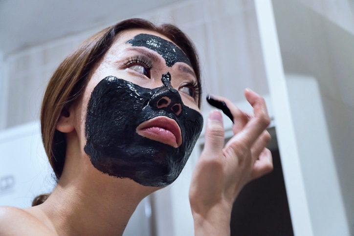 Woman peeling off - pulling off her charcoal black facial mask