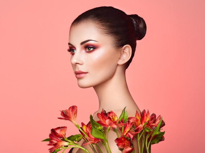 Portrait of beautiful young woman with Alstroemeria flowers. Brunette woman with luxury makeup. Perfect skin. Eyelashes. Cosmetic eyeshadow. Red flowers. Coral color