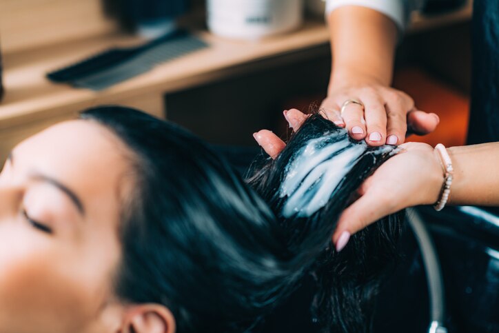 Young beautiful woman getting revitalizing hair treatment by female hairdresser in beauty salon.