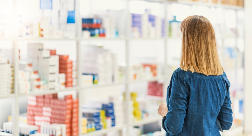 Medicine, pharmaceutics, healthcare and people concept - Panoramic Photo of young female customer choosing drugs at pharmacy. Rear view of Customer examining, looking for medicament in drug store.