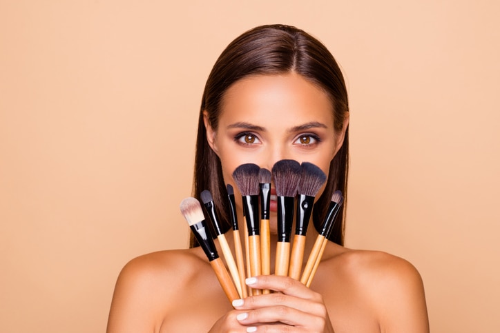 Close up portrait of brunette hair leisure lifestyle good-looking lovely pretty lady with her make up brushes shoulders she look at camera hide face isolated on pastel beige background