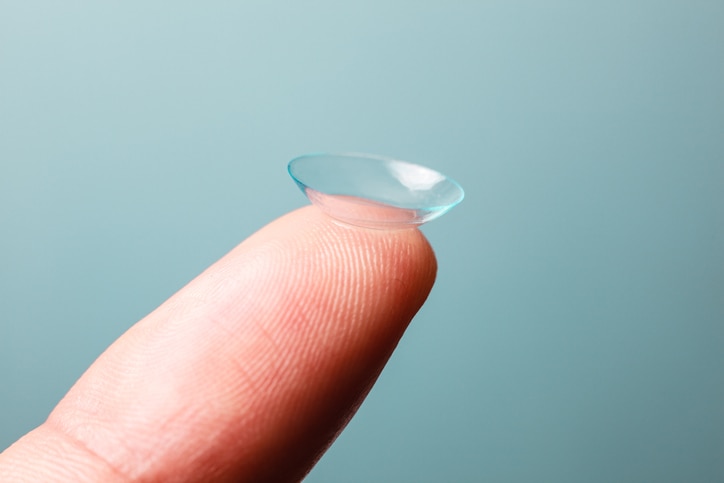 A Contact lens is resting on a finger against a blue background