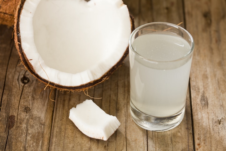 "A high angle close up of half a coconut and a tumbler full of coconut water, coconut water is said to be rich in potassium and antioxidants. Shot on a grungy old wooden table."