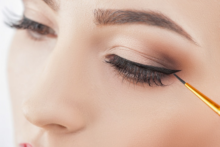 Close up of female eyes. The young woman is applying the eyeliner on her eye