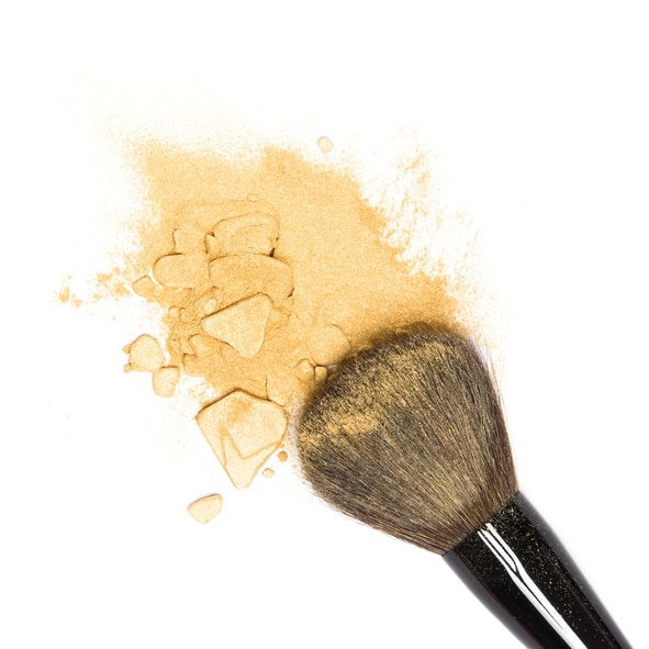 Close-up of crushed mineral shimmer powder golden color with makeup brush on white background