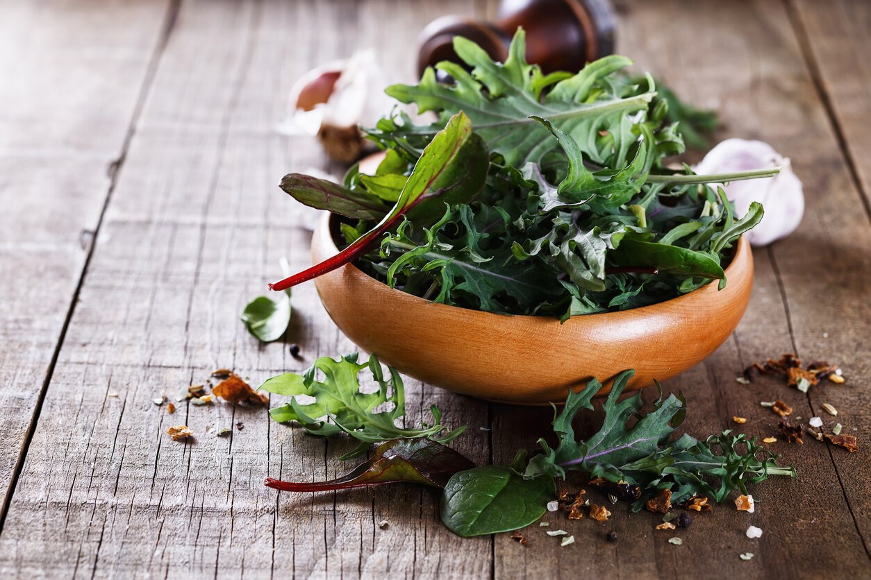 Leafy green mix of kale, spinach, baby beetroot leaves over rustic wooden background