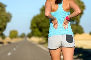 Female runner athlete low back injury and pain. Woman suffering from painful lumbago while running in rural road.