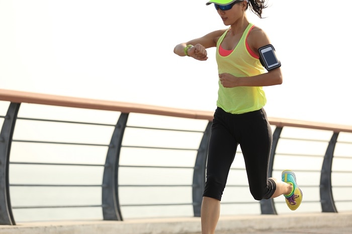 young fitness woman runner checking her running time from smart watch at seaside