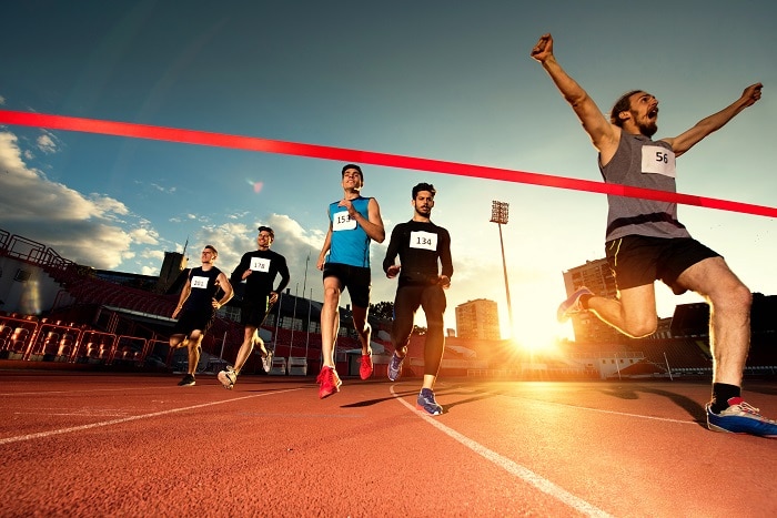 Low angle view of young happy man celebrating his success after crossing the finish line and winning the race before other athletes.