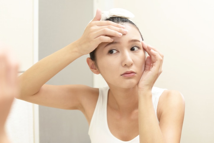 Asian woman looking at her face in mirror