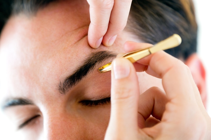 Portrait of man removing eyebrow hairs with tweezing.