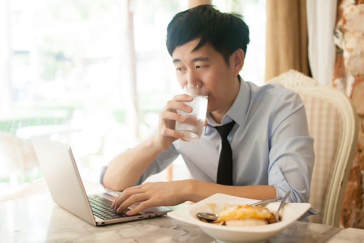 Young Asian man working while eating with his laptop in restaurant