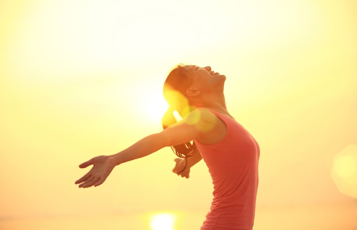 cheering woman open arms under sunrise on beach