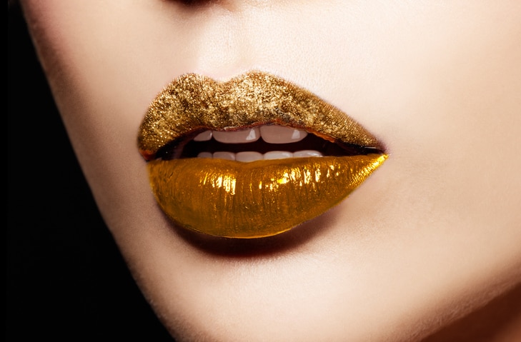 Closeup of gold artistic lips. Glitter upper lip and shiny lower lip. Makeup cosmetic image.