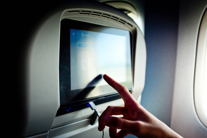 A teenage boy pressing the touchscreen on an aircraft backrest to choose films on a long haul flight.