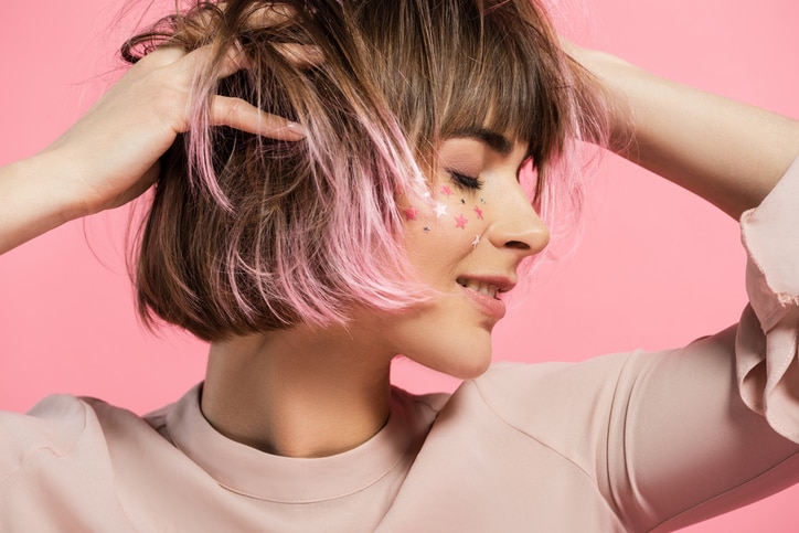 Young attractive woman with pink stars on her face posing with hands in hair and eyes closed