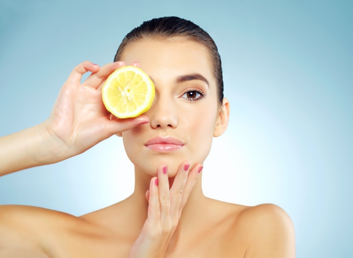 Studio portrait of a beautiful young woman covering her eye with a lemon against a blue background