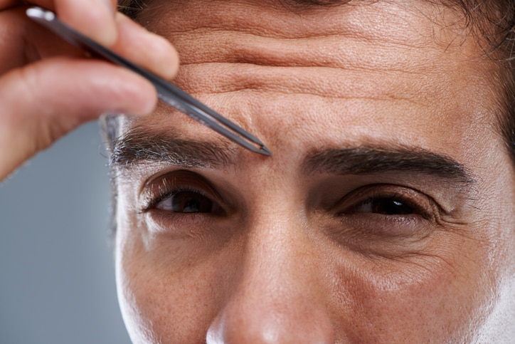 A young man tweezing the hair on his face