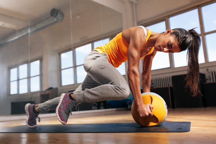 Fit female doing intense core workout in gym. Young muscular woman doing core exercise on fitness mat in health club.