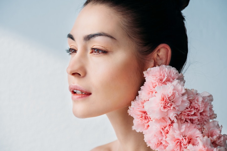 Portrait shot of beautiful woman with no makeup posing with a bouquet of flowers near her face